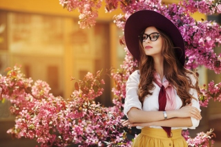 ピンクの桜、梅の花の前にメガネをかけた凛とした女性が立っている