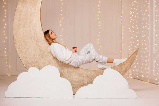 月の模型の上に女性がパジャマ姿で座っている