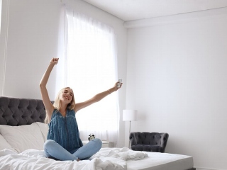 ベッドの上でエアコンのリモコンを手に、伸びをする女性
