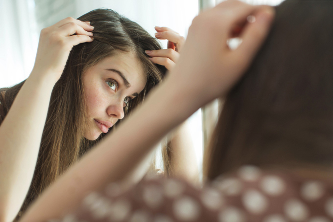 女性が髪の毛の生え際を鏡でチェックしているイメージ画像