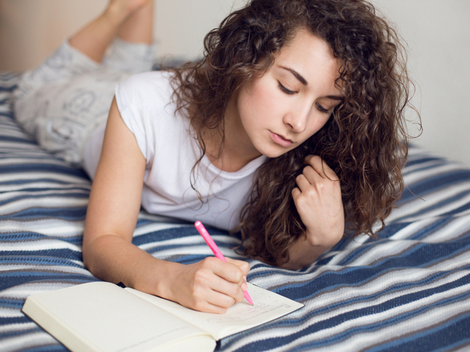 女性がベッドで日記を書いている画像