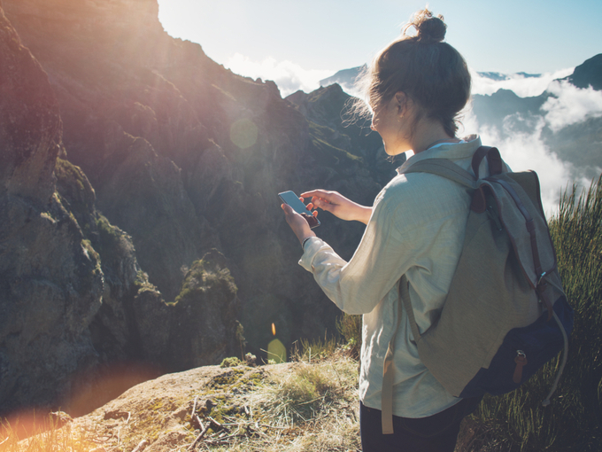 山でスマートフォンを見ている女性の画像