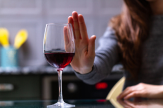 女性がワインの前に手を掲げ、飲酒を拒否している画像