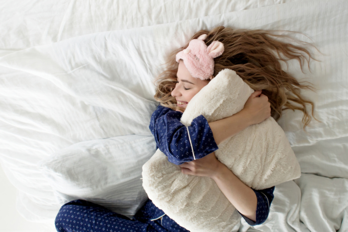 枕を抱き抱えて笑顔で寝ている女性