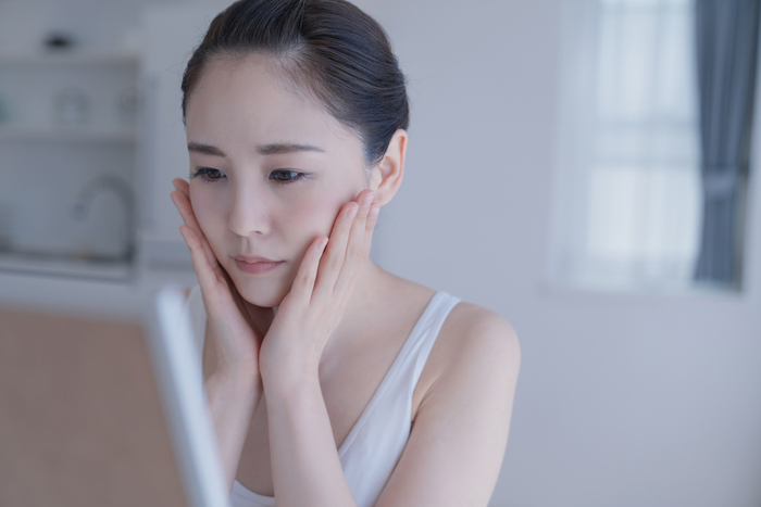 不安げに肌に手を当てて鏡をみる女性