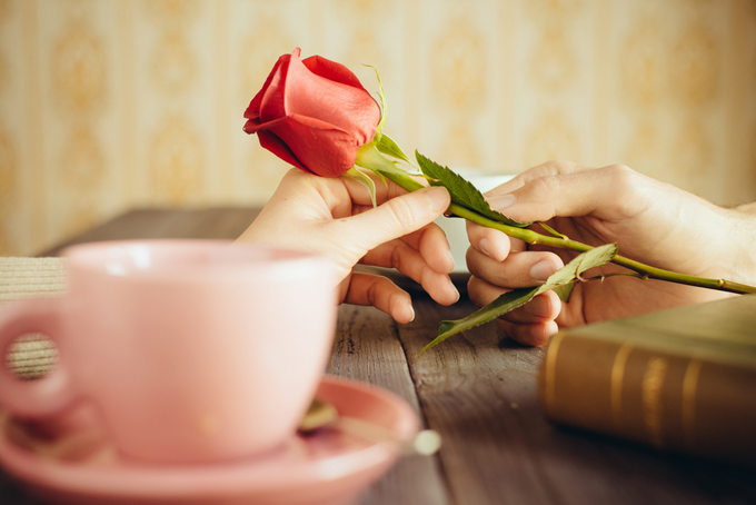 テーブルの上にピンクのカップと手に一輪のバラの花を持っている