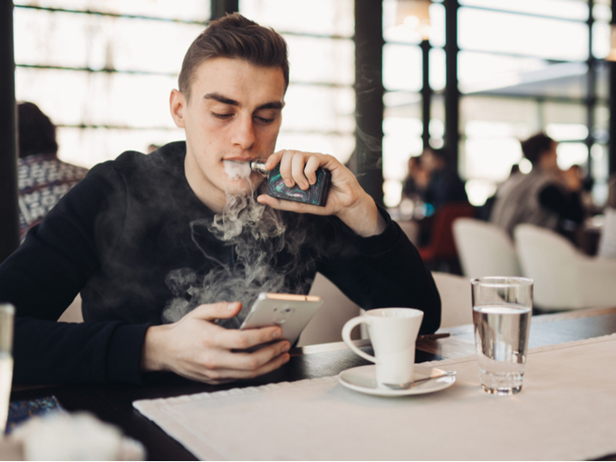 カフェで電子たばこを吸う若者