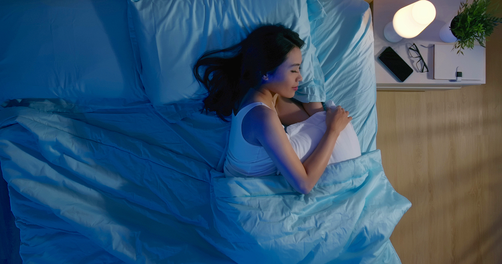 部屋を暗くしたブルーのベッドで横向きに寝ている女性