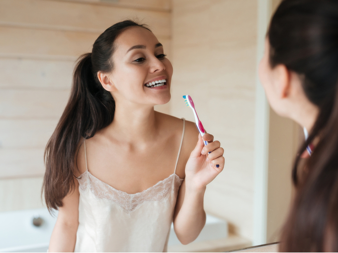歯ブラシをもって鏡で口もとをチェックする女性
